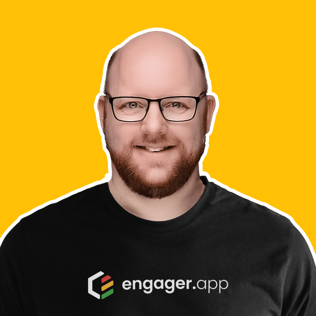 A person with a beard and glasses is smiling. They are wearing a black shirt with the text engager.app on it. The background is bright yellow.