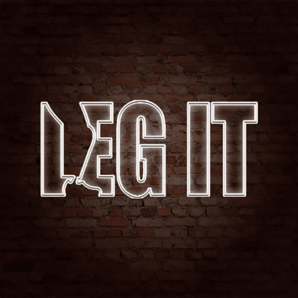 The phrase LEG IT is displayed in bright white neon lights against a dark red brick wall. The letter L is styled with a leg design, making it appear dynamic and illustrative.