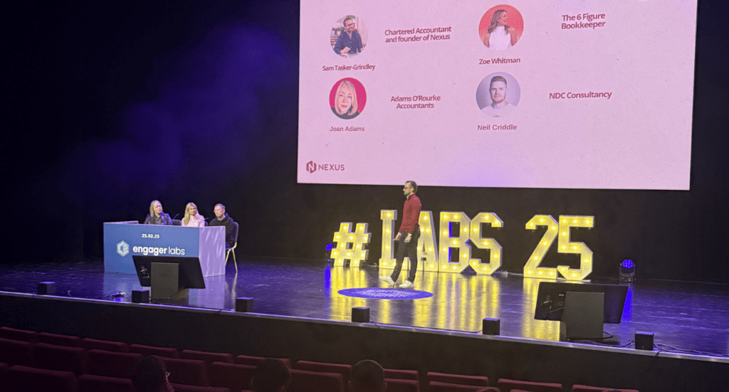 Sam Tasker-Grindley of Nexus by Sedulo stands on stage near a large #LABS 25 sign, addressing an audience about the power of collaboration. Behind him, a screen displays headshots and names of fellow speakers. A panel of three people is seated at a table to the left, under the engager labs logo.