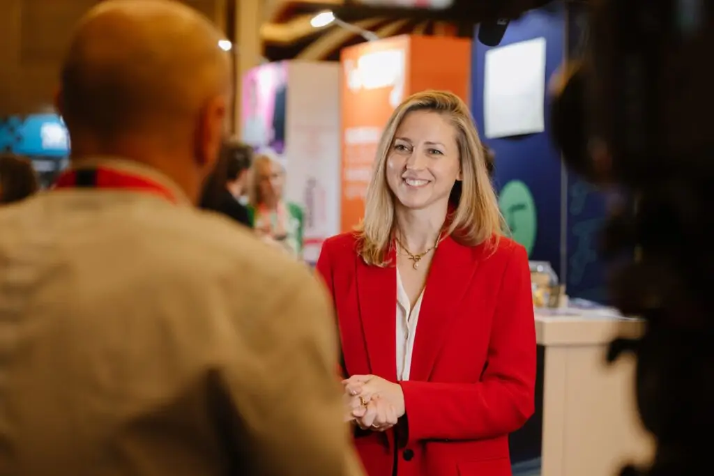 Ami Copeland in a red blazer talking with a visitor at an event